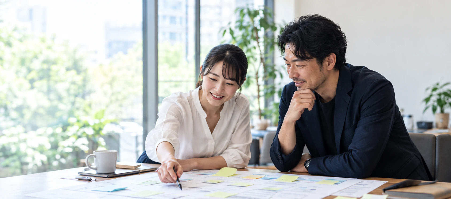 明るいオフィスで、業務の図面を囲んで相談する二人